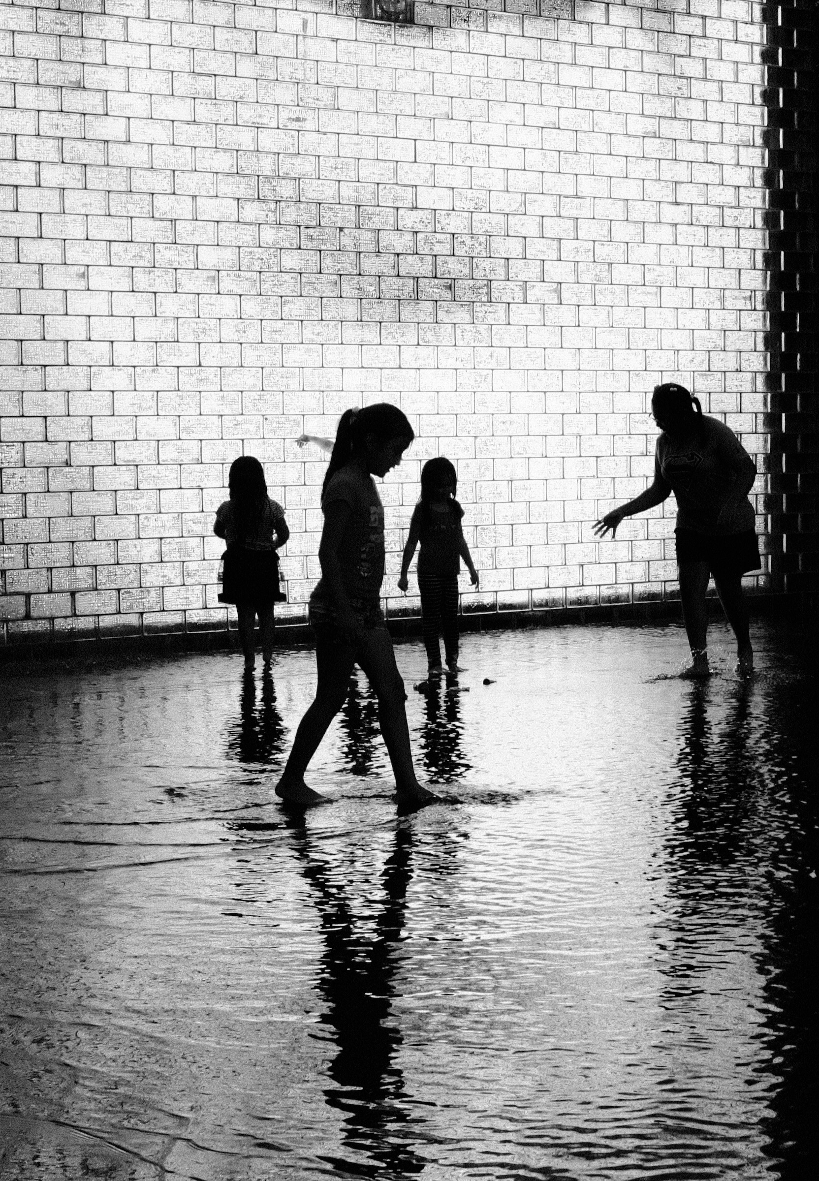 Children and young girls splashing joyfully in the shallow reflection pool of Crown Fountain in Millennium Park Chicago